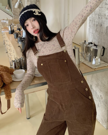 Une femme prenant une pose les bras ouverts mettant sa combinaison en velours de couleur marron s'appuyant sur une table avec des cafetières en arrière-plan