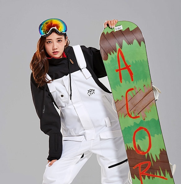 Salopette de ski pour femme à bretelles et snowboard vert dans une main.