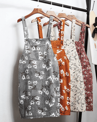 Robes salopettes en velours à motifs à fleurs, de différentes couleurs sur des ceintres sur un portant avec un chapeau de paille sur le côté.