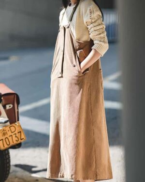 Femme portant une robe salopette en velours côtelé beige anple avec plusieurs poches, dans la rue devant l'arrière d'une moto.