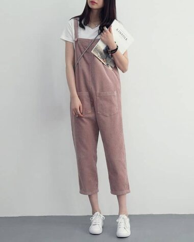 Photo d'une femme portant une combinaison en velours côtelé rose, longueur 7/8me avec un t-shirt blanc, des baskets blanches, et un magazine à la main.