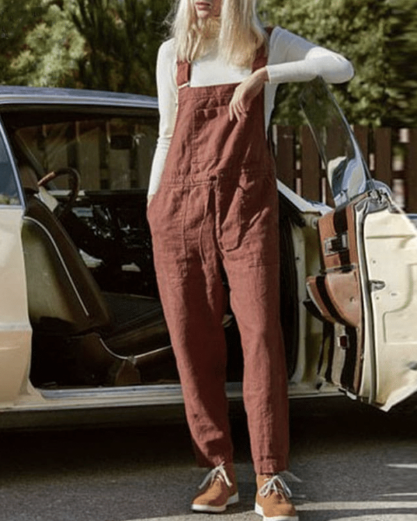 Femme accoudé à la portière d'une voiture vintage, portant une salopette ample, couleur rouille, avec un cordon à la taille et un haut à manches longues blanc.