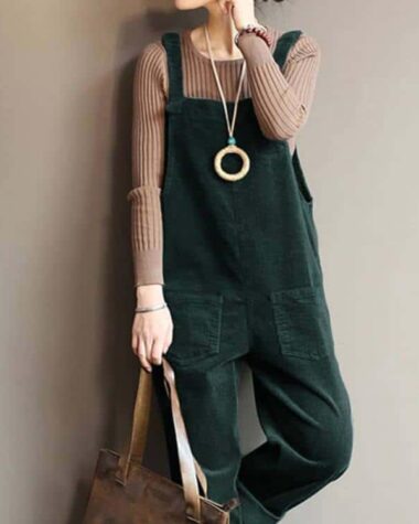 Femme appuyée contre un mur portant une salopette verte et un sous pull beige