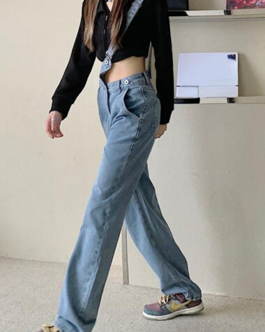 Femme marchant dans un appartement portant une salopette pantalon en jean avec une seule bretelle, des baskets et un top noir