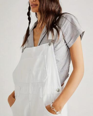 Salopette blanche femme tendance avec poche centrale et poches latérales, portée avec un chemisier gris sous la salopette.