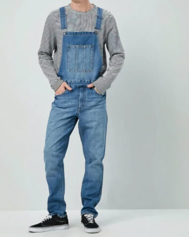 Salopette jeans style libre et urbain bleu ou bleu ciel, portée par un jeune vêtu d'un t-shirt rayé à manche longue.