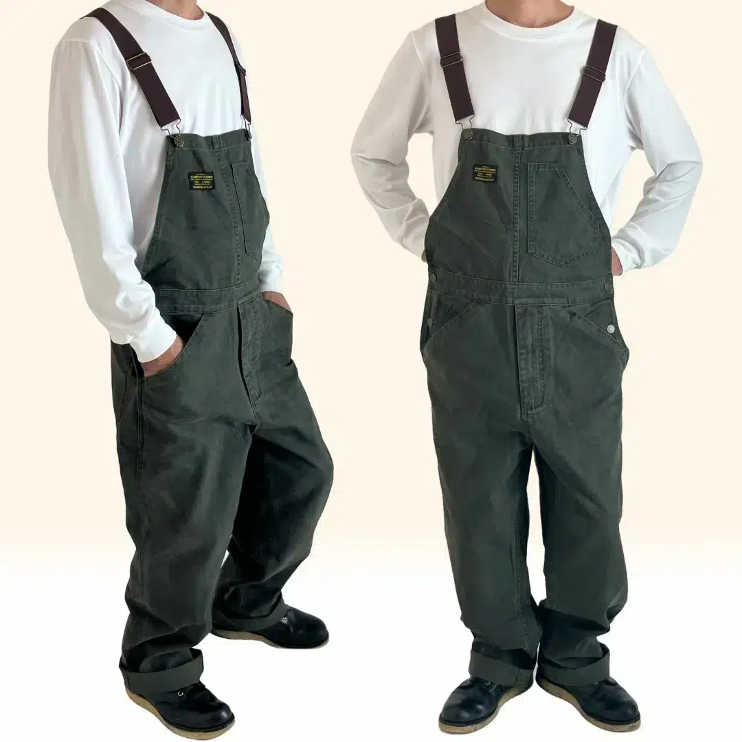Salopette travail vintage homme 1 Salopette travail vintage homme de couleur kaki en coton avec bretelle marron portée par un jeune homme vêtu d'un t-shirt blanc.