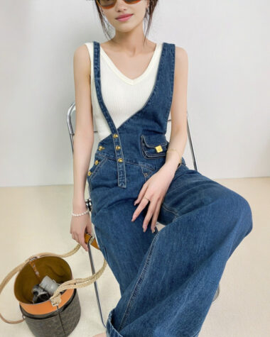 Salopette pour femme design asymétrique unique en jean bleu marine avec jeu de bretelles décalées et poche plaquée avec fermoir doré.