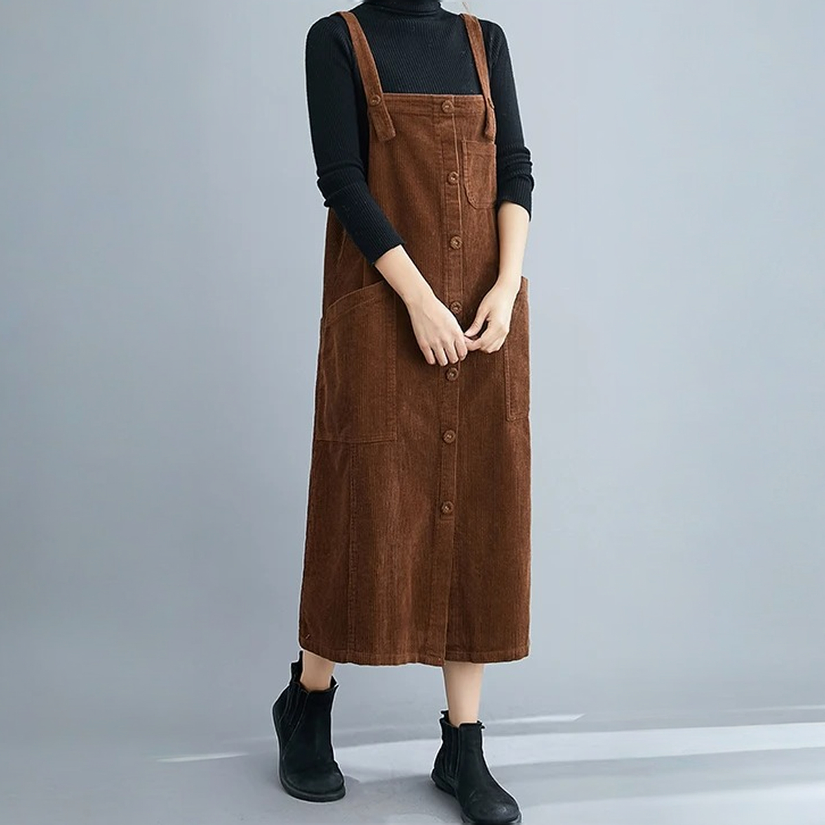 Robe salopette en velours mi-longue marron portée avec un col roulé par une jeune femme caucasienne